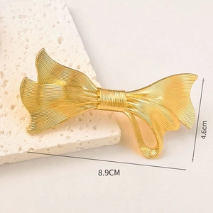Detail view of a 8.9cm gold bow hair claw clip with linear texture on a stone prop