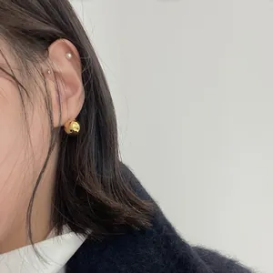 Detailed view of polished golden ball studs styled with pearl earrings on a model