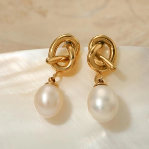 Elegant gold knot earrings with natural freshwater pearl drops on marble background