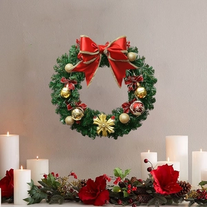 Christmas wreath with green pine branches, red silk bow, and gold ornaments on a beige wall