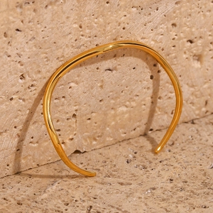 Detailed view of irregular wave gold bangle on natural stone background with high polish