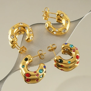 Detailed view of two pairs of C-shaped gold hoop earrings with clear and colorful crystals