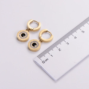 Detail of Roman numeral gold earrings with black stone next to a measuring ruler