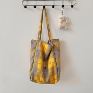 Detail of large yellow plaid canvas tote bag with woven texture and leather brand patch