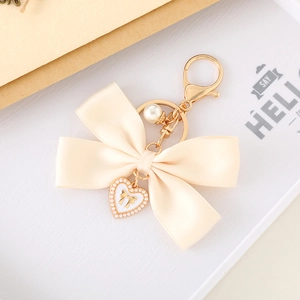 Detailed macro view of cream satin bow keychain with gold heart charm and pearl drop