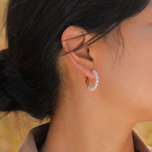 Close-up of elegant gold stainless steel C-shape earrings featuring small white pearls