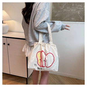 Detail of drawstring closure and apple graphic on minimalist cream canvas tote bag