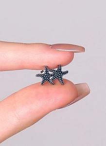 Macro view of starfish stud earrings with vintage silver grain texture held by fingers