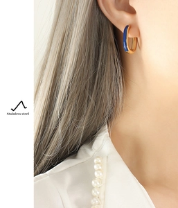 Detail of model wearing gold and blue enamel stainless steel hoop earrings on the ear