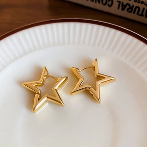 Detailed shot of gold star-shaped earrings on a decorative white ceramic plate