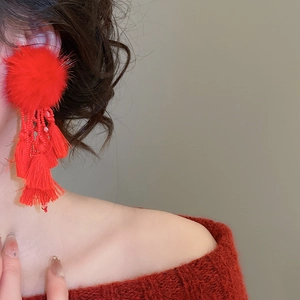 Detailed view of red pompom and layered fabric tassel earrings on a model wearing a sweater