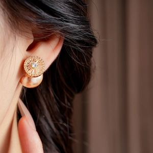 Close-up of gold plated pearl earrings with zircon inlay worn by a model in soft light