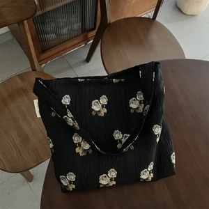 Detail of black textured tote bag with vintage white rose jacquard and side brand tag