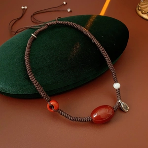Detailed close-up of handmade wax rope necklace with red agate beads on green velvet