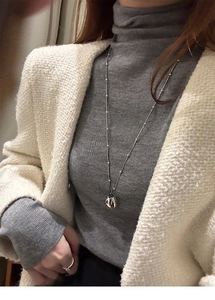 Silver minimalist irregular metal pendant on a long bead chain over a grey sweater