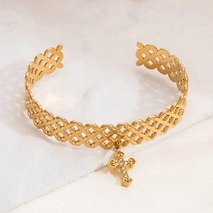 Detail of golden open bangle with cross charm and zircon inlay on a stone background