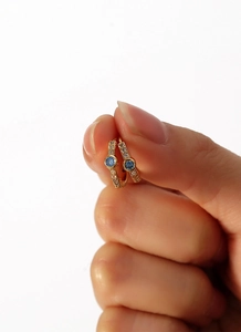 Close-up of gold hoop earrings with sparkling blue zircon center and pavé white stones