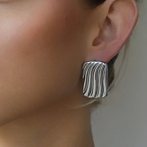 Boucles d'oreilles géométriques argentées avec texture ondulée sur un modèle