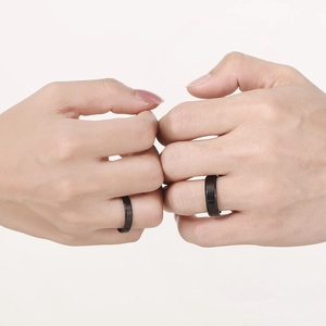 Close-up of minimalist black stainless steel rings worn by a couple on a beige backdrop