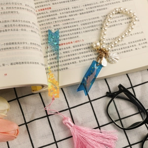 Detail of heart resin bookmark with pink tassel and whale starry bookmark on an open book