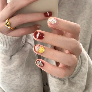Detail of dark red press-on nails featuring pearl accents and gold leaf foil art
