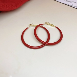Chic red enamel large hoop earrings with gold needles on a minimalist beige background