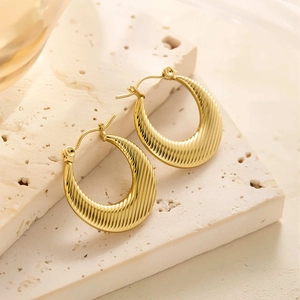 Gros plan de boucles d'oreilles créoles torsadées dorées 18 carats sur pierre beige