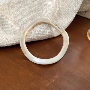 Detailed close-up of amber resin bangle with cream marble patterns on dark wood