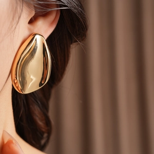Close-up of polished gold teardrop earring with high-gloss metallic finish on model