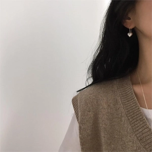 Close-up of minimalist sterling silver heart earrings worn by a model in warm knitwear