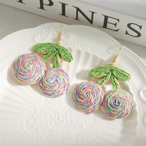 Detail of colorful woven cherry earrings with green leaves on white ceramic plate