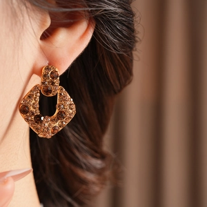Détail de boucles d'oreilles vintage en or avec strass bruns portées par un mannequin