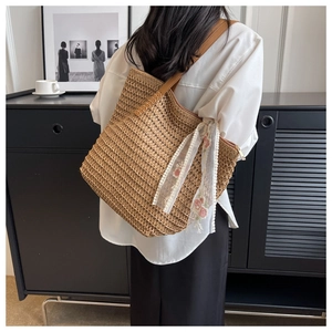 Brown woven straw bucket bag shown with leather strap and delicate lace scarf detail