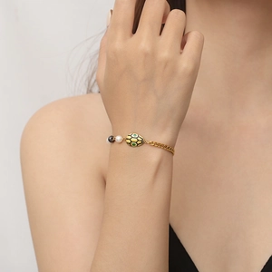 Gold-plated chain bracelet with green and yellow enamel beetle charm on female wrist