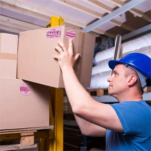 Fragile warning stickers on cardboard box in warehouse with professional warehouse staff