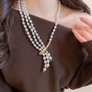 Detail of three-layer pearl necklace with golden irregular textured buckle and tassels