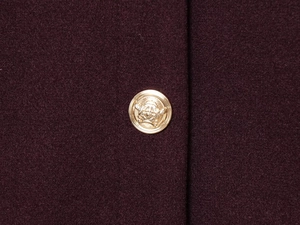 Detailaufnahme von dunkelburgunderfarbenem Wollstoff mit geprägten Goldmetallknöpfen