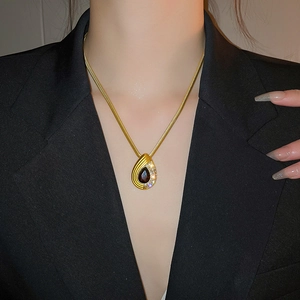 Detailed view of a gold snake chain necklace with a ruby red teardrop pendant on a model