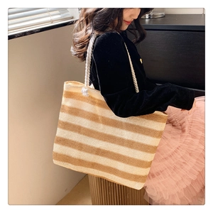 Detail of striped woven straw tote bag featuring thick white rope handles and large capacity