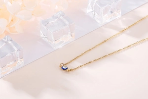 Macro shot of gold evil eye pendant with blue enamel on a delicate stainless steel chain