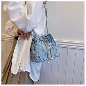 Blue denim bucket bag with gold chain and pearl accents worn over a white shirt