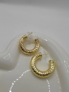 Detailed close-up of golden chunky hoop earrings with diamond-cut texture in a white tray