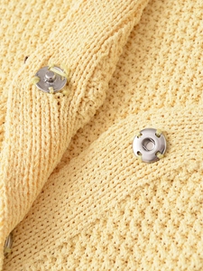 Close-up of yellow knitted fabric texture with silver metal snap button closure