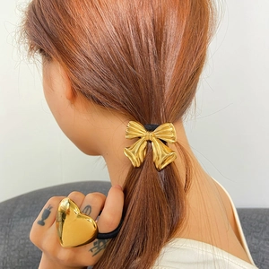 Golden heart and metal bow hair ties shown on a ponytail and held in hand for women