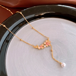 Detail of pink enamel flower necklace with faux pearl on gold chain in ceramic tray