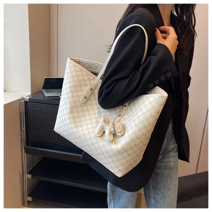 Beige tote bag with monogram pattern and bear charm shown on a model for scale