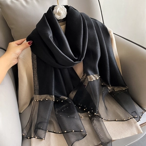 Elegant black silk scarf with golden thread and pearl beads laid on a sofa