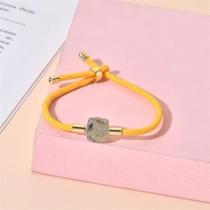 Détails de la texture du bracelet en corde jaune avec perles dorées et pierre carrée