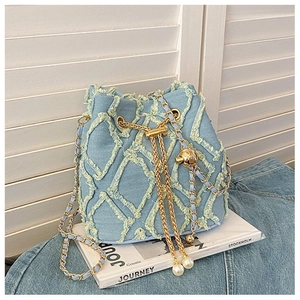 Detail of blue denim bucket bag with quilted frayed edges and pearl tassel charm