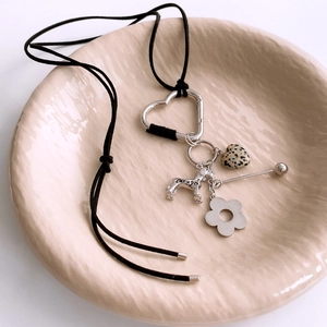 Detail of stone heart and metal dog charms on a black cord necklace in a ceramic dish